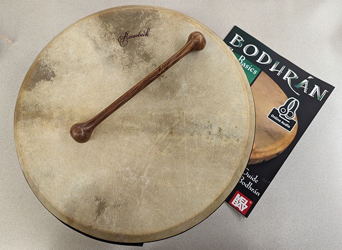 A photo of a 14 inch round drum with wooden striking mallet and music book.